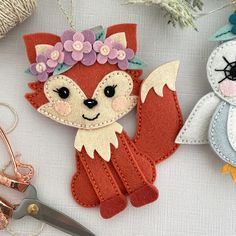 two handmade felt animals sitting next to each other on a table with scissors and thread