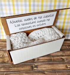 two white crocheted baby booties in a cardboard box on a wooden table