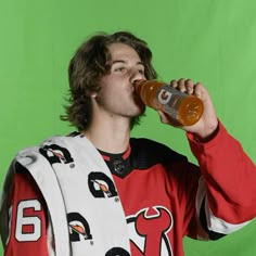 a young man drinking from a bottle while wearing a scarf around his neck on a green screen studio background