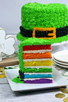 a slice of rainbow cake on a plate with a shamrock hat topper in the background