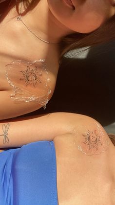 two women with sun and butterfly tattoos on their stomachs, both wearing blue swimsuits