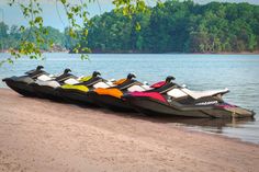 four jet skis lined up on the shore of a lake with trees in the background