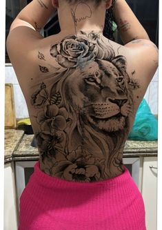 the back of a woman's body with tattoos and flowers on her head, behind which is a lion