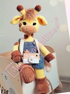 a stuffed giraffe is holding a camera in its hand and wearing overalls