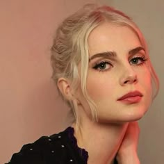 a woman with blonde hair and blue eyes is posing for a photo in front of a pink wall