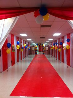 a red carpeted hallway with balloons and streamers hanging from the ceiling on either side