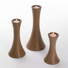 three wooden candlesticks sitting next to each other on a white surface with one candle in the middle