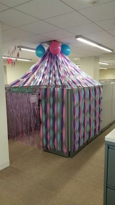 an office cubicle decorated with pink, blue and green streamers on the ceiling