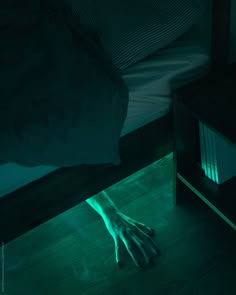 a person's hand on the floor in front of a bed with green light