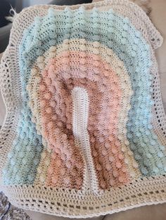 a crocheted blanket with a white hook in the center and multicolored yarn