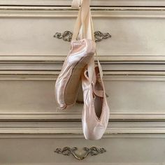 two ballet shoes hanging on a wall next to a drawer with drawers in the background