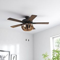 a ceiling fan in a white room with pictures on the wall and a potted plant