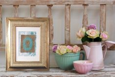 some pink and green vases with flowers in them next to a picture frame on a wooden bench