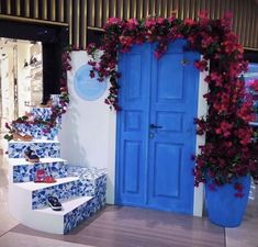 a blue door and some steps with flowers on the wall next to it in front of a store