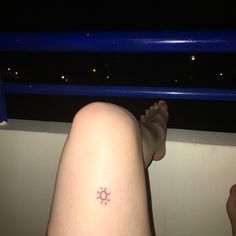 a person's foot with a small sun tattoo on their left leg, sitting next to a railing