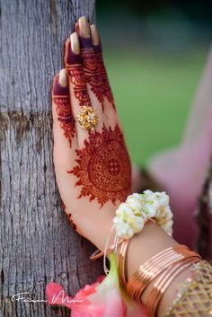 a woman's hand with henna on it and flowers in her bracelet next to a tree