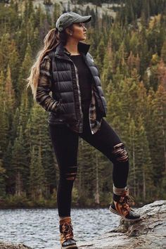 a woman standing on top of a rock next to a lake with trees in the background