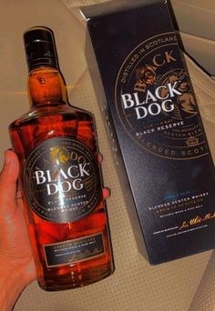 a hand holding a bottle of black dog whiskey next to a box on a table