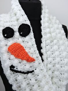 a crocheted snowman scarf with black eyes and an orange nose