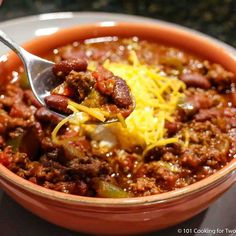 a spoon full of chili and cheese in a bowl