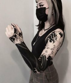 a woman with black and white tattoos on her arm wearing a face mask covering her mouth