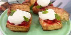 four pastries with strawberries and whipped cream on them sitting on a green plate