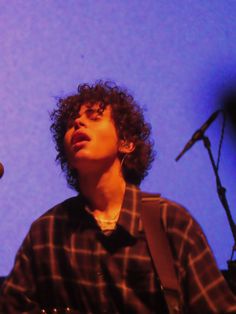 a young man with curly hair is playing the guitar in front of a microphone on stage