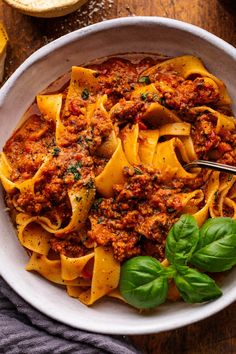 a white bowl filled with pasta and sauce on top of a wooden table next to bread