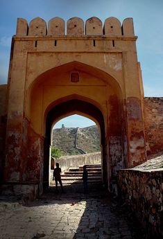 two people are standing under an arch in the stone wall with stairs leading up to it