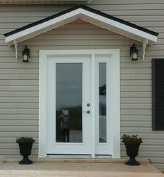 the front door of a house with two black planters on the porch and one person standing in the doorway