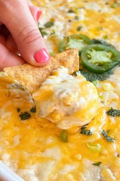 a person dipping cheese into a casserole with green peppers and jalapenos