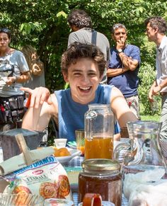 a young man sitting at a table with food in front of him and people around him