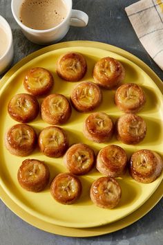 a yellow plate topped with small pastries next to two cups of coffee