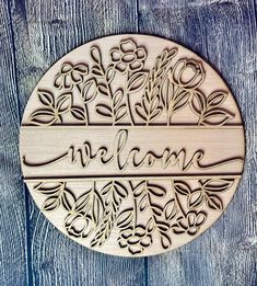 a wooden sign that says welcome with flowers and leaves in the center on a wood background