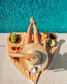 a woman laying on top of a towel next to a pool filled with fruit and vegetables