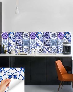 a kitchen with blue and white tiles on the wall, an orange chair and a black cabinet