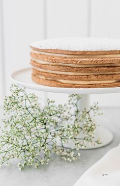 a stack of cookies sitting on top of a white cake platter next to a bouquet of baby's breath flowers