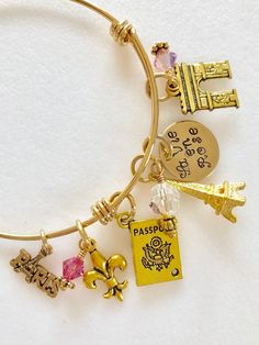 "Perfect souvenir of an enchanting trip to Paris, France. Adjustable gold plated bangle is highlighted with hand stamped quote \"La Vie en Rose\" and 5 detailed Parisian charms accented with rose colored Swarovski crystals AB. Adjustable bangle is made of heavy gold plate over 1.8mm stainless steel. It is hypoallergenic and tarnish resistant. The diameter is 2 1/2\" to fit most. Hand stamped 5/8\" 24 gauge shiny brass disc reads \"La Vie en Rose\". Two 6mm rose colored Swarovski crystals AB and Gold Charm Bracelet As A Souvenir, Adjustable Gold Charm Bracelet For Personalized Gift, Pink Jewelry With Charms For Personalized Gift, Gold Nickel-free Charm Bracelet For Personalized Gift, Handmade Gold Charm Bracelet For Mother's Day, Nickel-free Gold Jewelry For Best Friend Gift, Adjustable Charms Jewelry Souvenir, Adjustable Charms Jewelry As Souvenir, Pink Gold Bangle Jewelry Gift