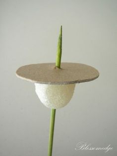 a green plant with a white ball on it's end and a piece of wood sticking out of the top