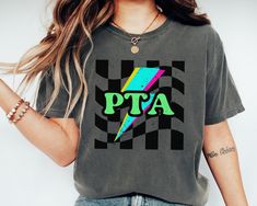 Embrace retro vibes with this stylish relaxed fit Comfort Colors® "PTA" T-Shirt featuring a vibrant lightning bolt design against a bold black and white checkered background. Perfect for casual wear, this eye-catching tee combines elements of nostalgia and modern pop culture. Crafted from high-quality material, it ensures comfort and durability. Great for PTA parents to show pride on or off campus.  Product Details:  - All items are unisex in the store  - Made with medium fabric (6.1 oz) - Relax Pta Board Shirts, Pta Shirts, Pta Gifts, Lightning Bolt Design, Pta School, Bold Black, Retro Vibe, Types Of Shirts, Comfort Colors