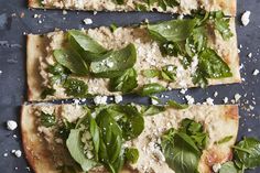 two flatbread pizzas with spinach and cheese on top, one topped with fresh basil