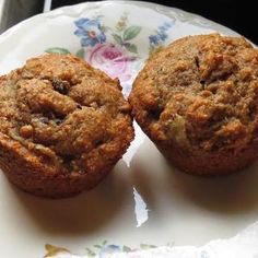 two muffins sitting on top of a white and blue flowered paper plate