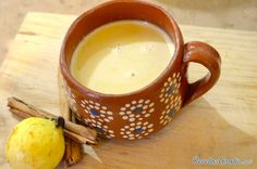 a cup filled with liquid next to an apple and cinnamon stick on a wooden table