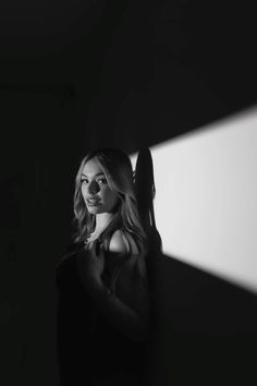 black and white photo of woman in dark room with light coming from behind her head