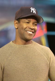 a man in a new york yankees hat smiles while standing next to a television screen