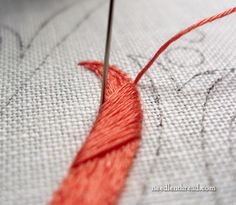 an orange thread is being sewn on a white piece of fabric with a red needle