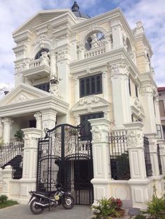 a motorcycle is parked in front of a large white building with iron gates and wrought iron railings