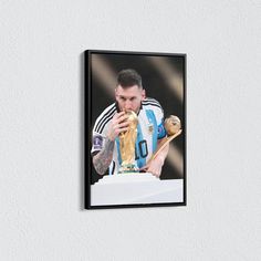 a framed photograph of a man eating a soccer ball and holding a golden trophy in his right hand