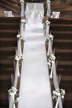 the aisle is decorated with white flowers and ribbons