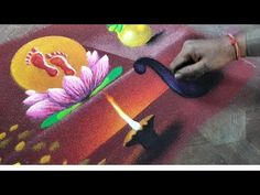 a person is painting on the ground with flowers and leaves in it, while another hand reaches for something